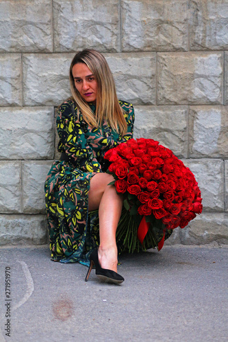a girl in a green dress with a bouquet of red roses at the concrete wall