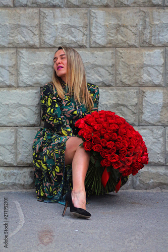 a girl in a green dress with a bouquet of red roses at the concrete wall