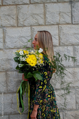 a girl in a green dress with a bouquet of yellow flowers at the concrete wall