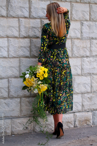 a girl in a green dress with a bouquet of yellow flowers at the concrete wall