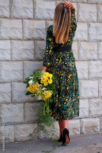 a girl in a green dress with a bouquet of yellow flowers at the concrete wall