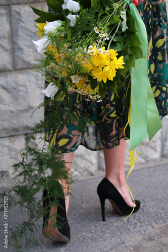 a girl in a green dress with a bouquet of yellow flowers at the concrete wall