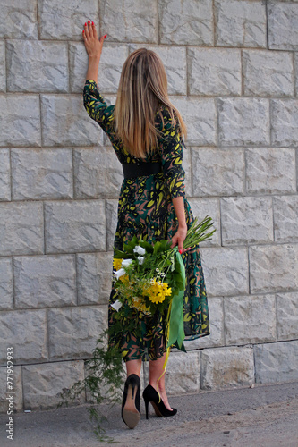 a girl in a green dress with a bouquet of yellow flowers at the concrete wall
