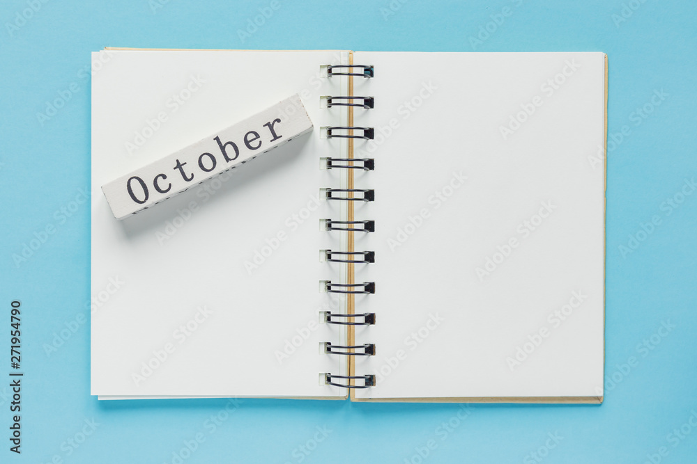 Clean spiral note book for notes and messages and october wooden calendar bar on blue background. Minimal business flat lay