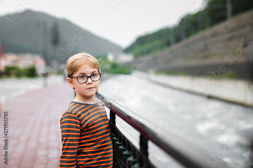 Strong, smart and funny little boy playing outdoors, wearing eyeglasses. Problem with eyes, astigmatism