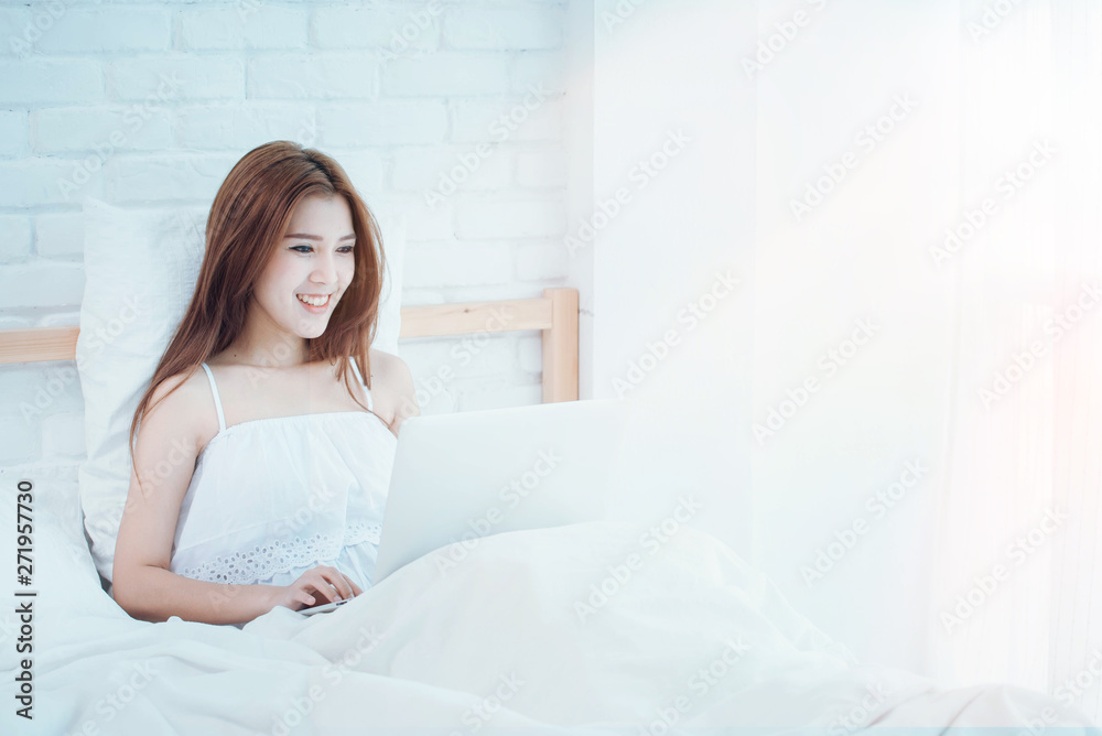 Happy woman reading news as she relaxes in bed with a laptop computer in the morning Happy woman reading news as she relaxes in bed with a laptop computer in the morning