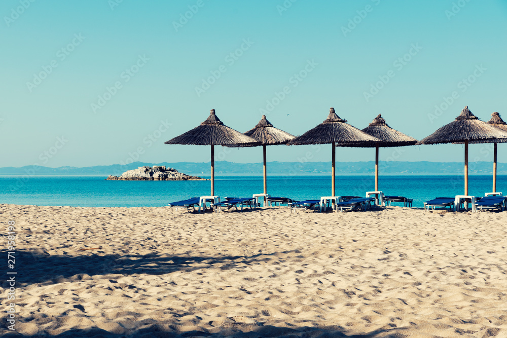 Beautiful beach in Halkidiki with straw parasols and rock on a horizon. Selective focus
