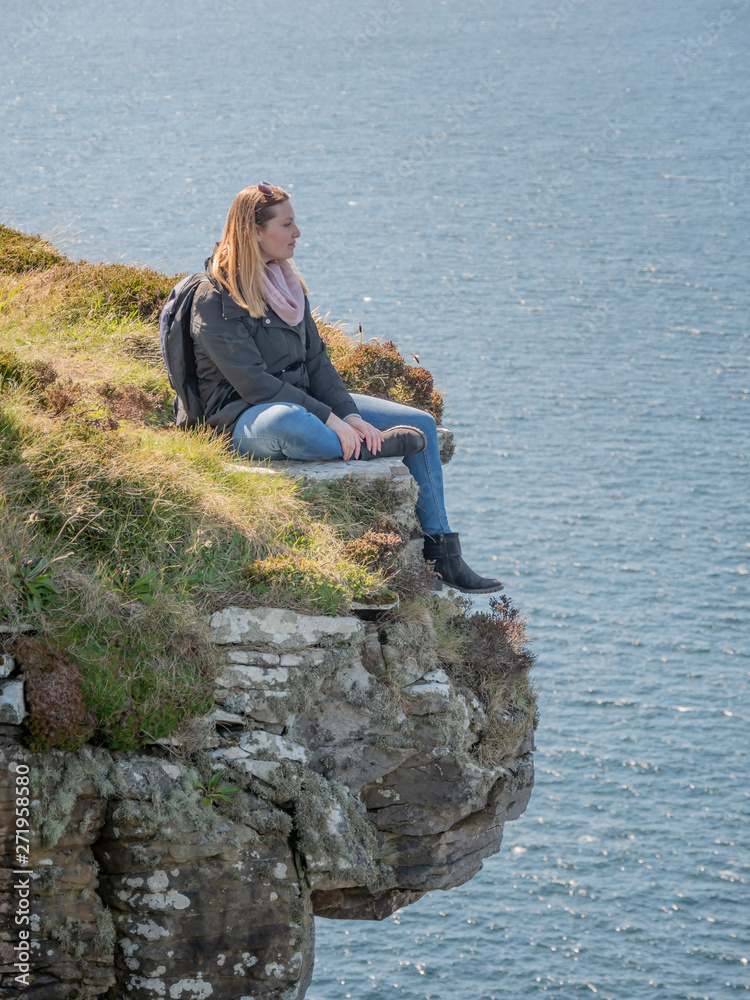 Young woman sitting on the edge of a cliff at the Irish west coast - travel photography