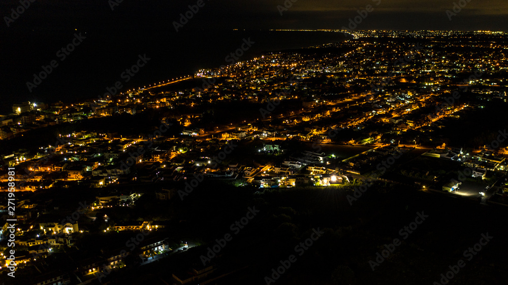 Aerial night view of the city and sea of ​​Anzio, near Rome, Italy. The lights of street lamps, car headlights and houses illuminate the urban landscape.