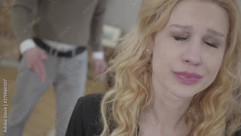 Pretty blond woman in the foreground crying, an emotional angry man yelling and shouting on the background. The couple has a quarrel. Difficulties in relationship Pretty blond woman in the foreground crying, an emotional angry man yelling and shouting on the background. The couple has a quarrel. Difficulties in relationship