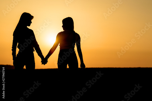 Silhouette two girl holding hand and walking in sunset. Young women on the beach. Lesbian couple near sea.