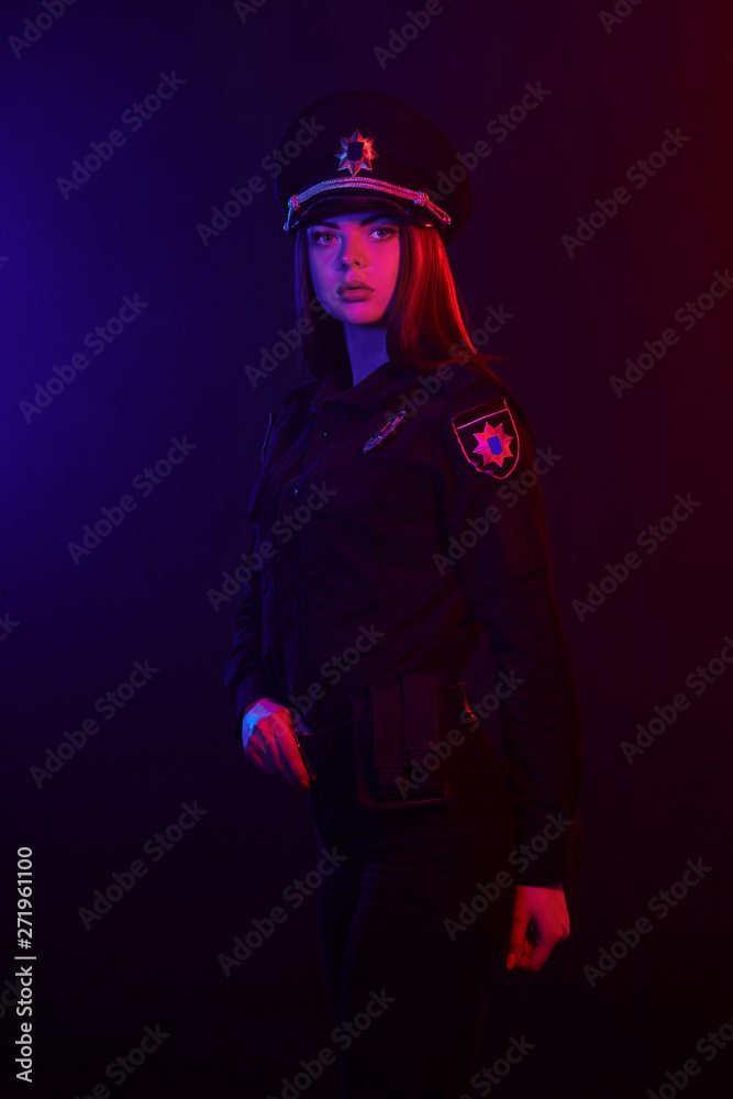 Redheaded female police officer is posing for the camera against a black background with red and blue backlighting. Redheaded female police officer is posing for the camera against a black background with red and blue backlighting.