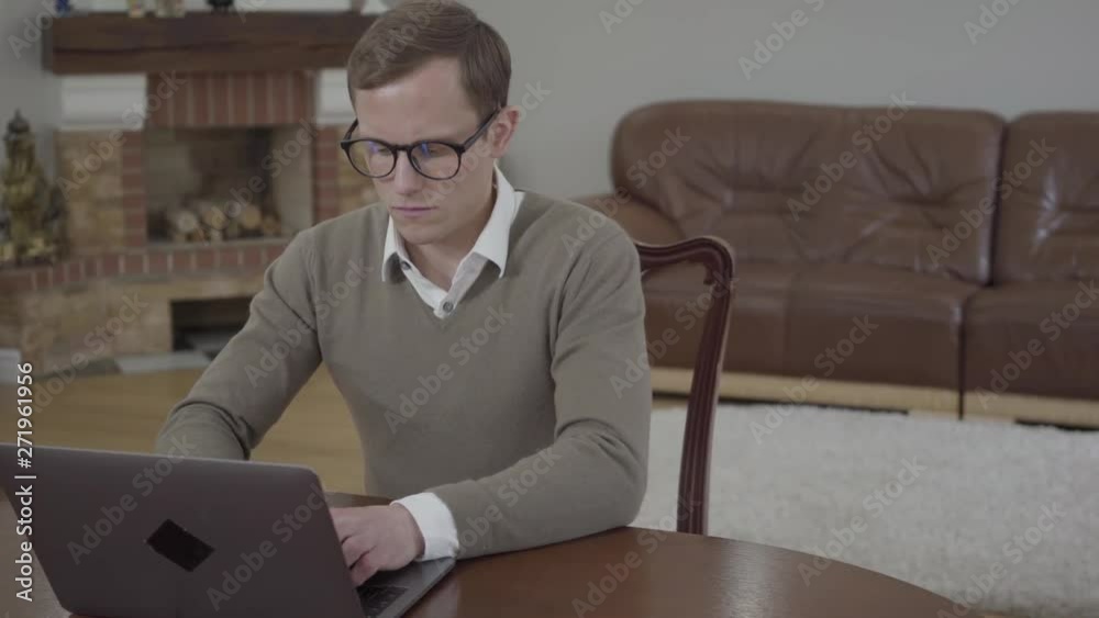 Young modestly dressed man in glasses sitting at the wooden table in the office working on his laptop. Unrecognizable angry woman bringing and throwing on the desk stack of books Young modestly dressed man in glasses sitting at the wooden table in the office working on his laptop. Unrecognizable angry woman bringing and throwing on the desk stack of books