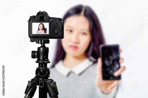 Focus on live view on camera on tripod, teenage girl with blurred scene in background. Teenage vlogger livestreaming show concept