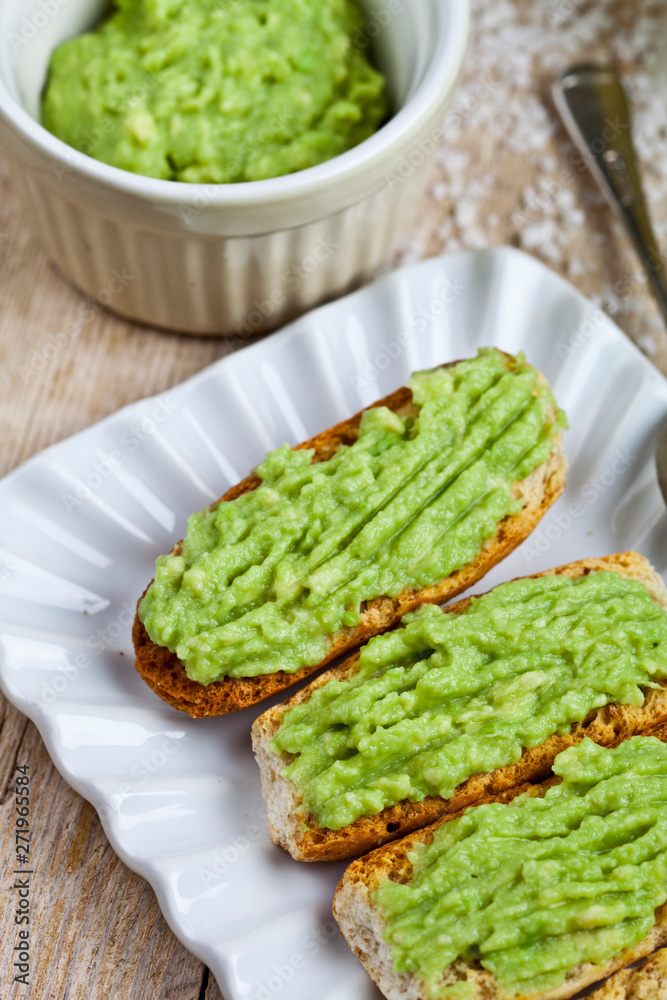 Fresh crostini with avocado guacamole on white plate closeup on rustic wooden table.