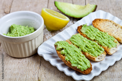 Crostini with avocado guacamole on white plate closeup on rustic wooden table. Diet breakfast. Delicious and healthy plant-based food.