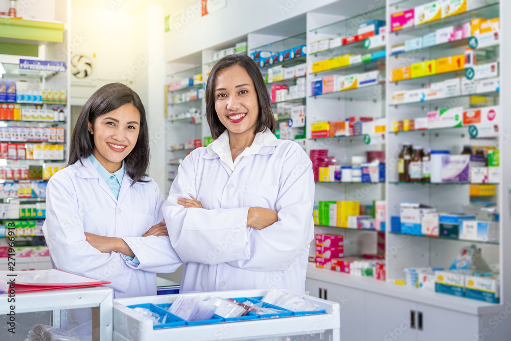 Two smiling asian pharmacists crossing arms while staying in drugstore. Medicine, pharmaceutics, health care and people concept. 