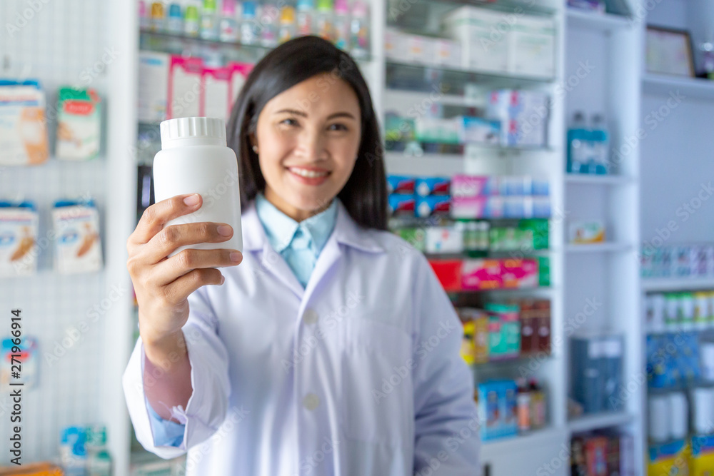 Smiling Asian female pharmacist holding medicine bottle in clinic or pharmacy. Medicine, pharmaceutics, health care and people concept. 