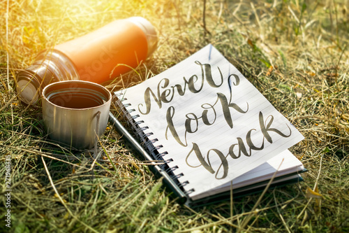 Never look back word written in white notebook with pen and red cup thermos on the green grass. Outdoor Concept hand writing showing Never Look Back, No regrets photo