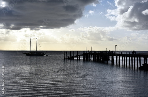 Kingfisher Bay pier at sunset. Moored sailboats and yachts in the bay. Silhoutette of people on the pier. World Heritage-listed Fraser Island is the world’s largest sand island. © katacarix