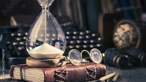 Moving sand in an hourglass, old diary and binocular, retro style photo