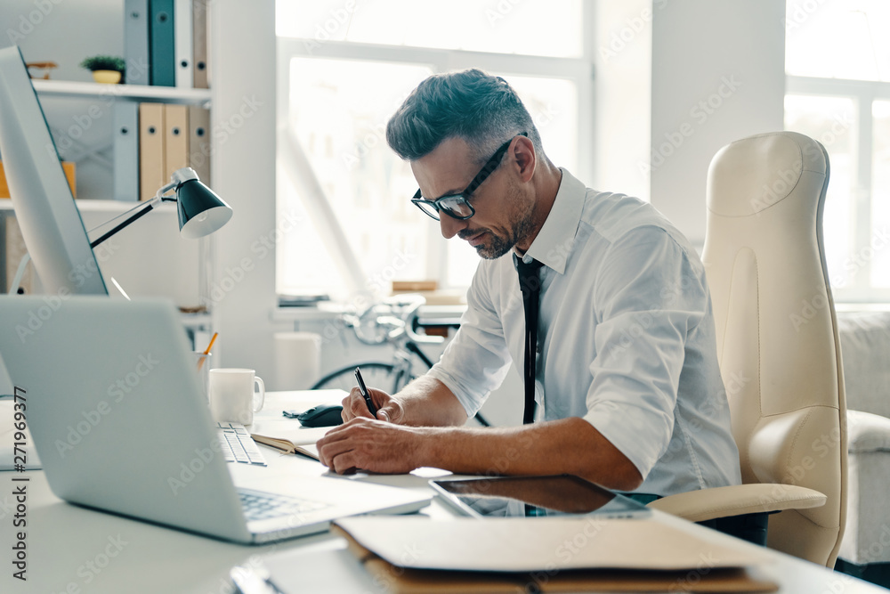Busy with paperwork. Good looking young man filling the forms while sitting in the office Busy with paperwork. Good looking young man filling the forms while sitting in the office