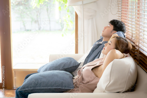 Young asian couple smile relax comfortable on sofa in the living room in holiday, family leisure and resting with happy in vacation on couch at home, lifestyle and wellbeing concept.