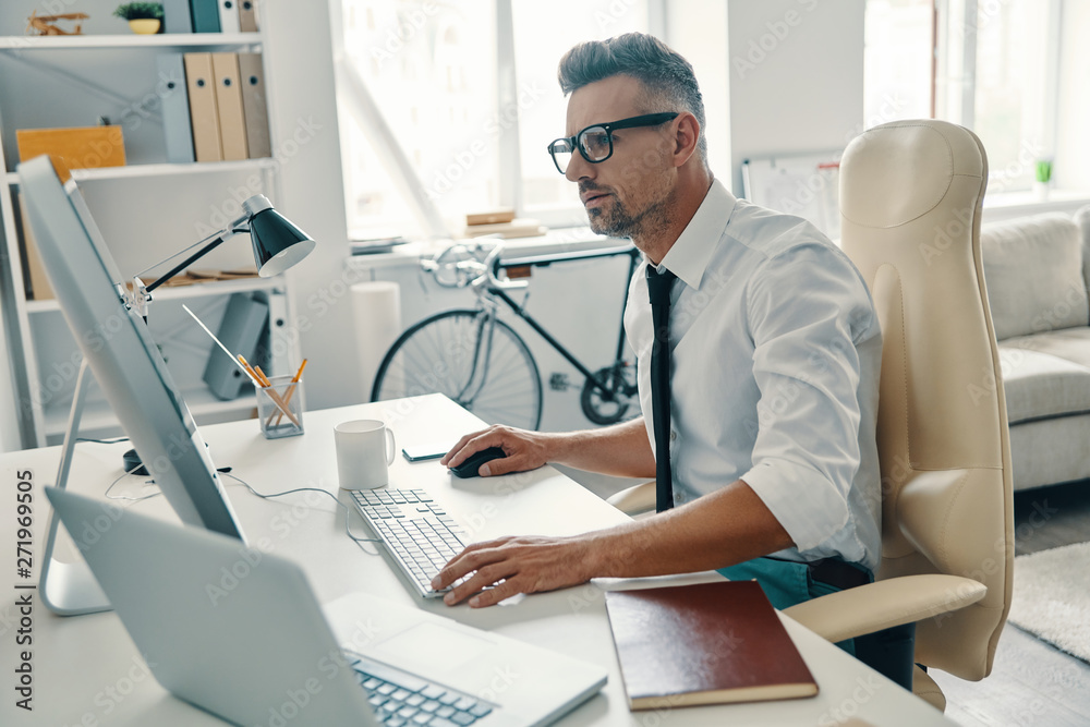 Putting ideas into something real. Thoughtful young man in shirt and tie working using computer while sitting in the office Putting ideas into something real. Thoughtful young man in shirt and tie working using computer while sitting in the office
