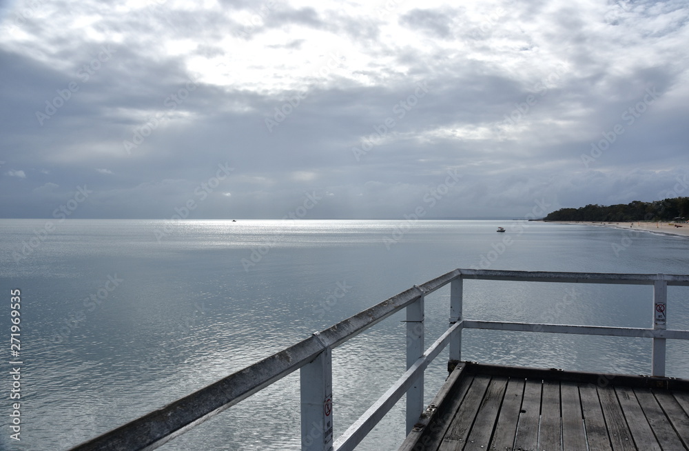 Obraz premium Gushing sea on a cloudy day. Horizontal view of dramatic overcast sky and sea. Fifty shades of blue and gray. View from a wooden pier.