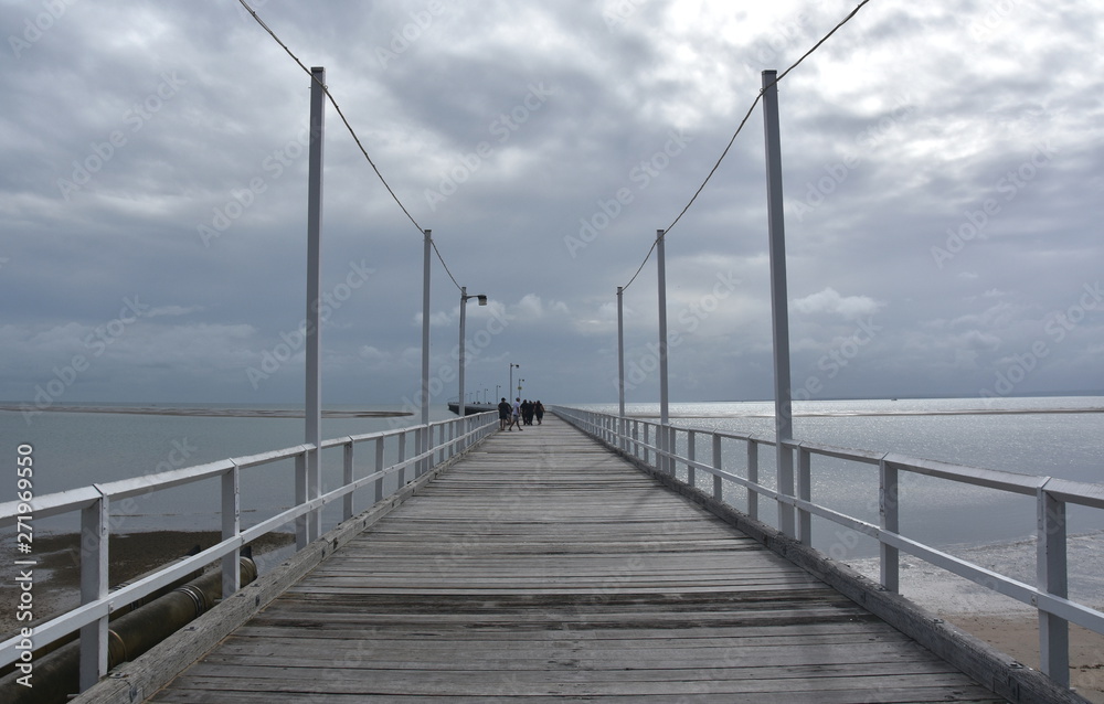 Great views of Hervey Bay from the wooden Urangan pier. The pier is also a popular fishing spot at all tides. Gushing sea on a cloudy day. Horizontal view of dramatic overcast sky and sea.