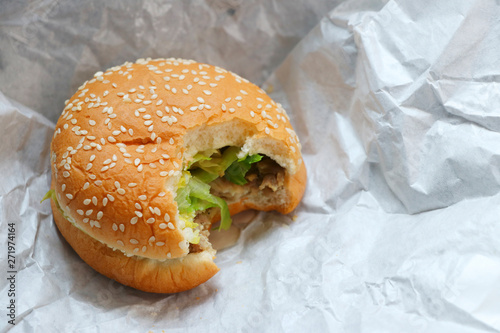 Hamburger with bite marks placed on white paper.