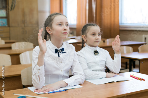 The schoolgirl girl raises her hand to answer the teacher's question, the second girl does not know the answer. Children sit in school, one raises his hand. photo