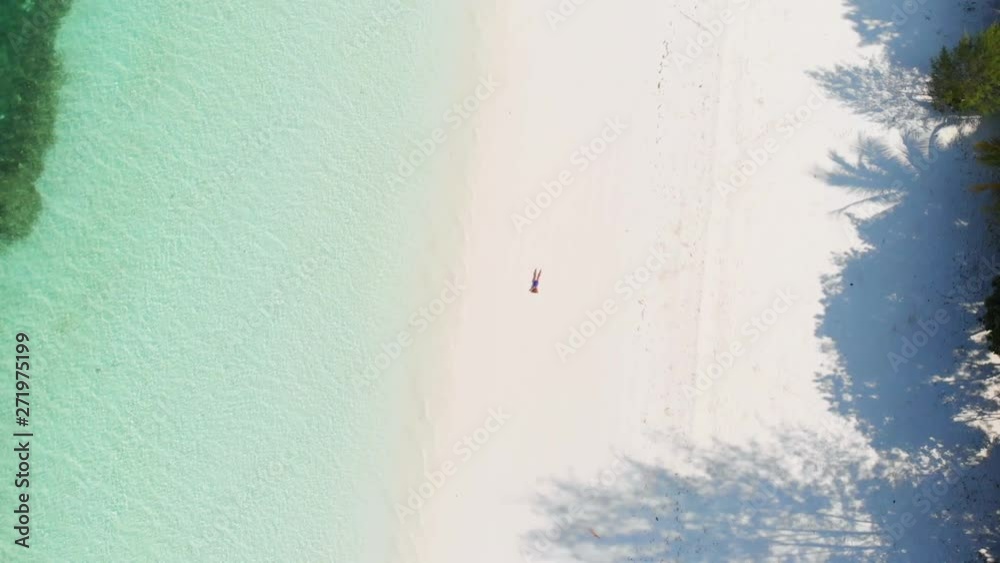 Aerial: Woman relaxing on white sand beach turquoise water tropical coastline Pasir Panjang Kei Islands Indonesia Moluccas Maluku Indonesia travel destination Aerial: Woman relaxing on white sand beach turquoise water tropical coastline Pasir Panjang Kei Islands Indonesia Moluccas Maluku Indonesia travel destination