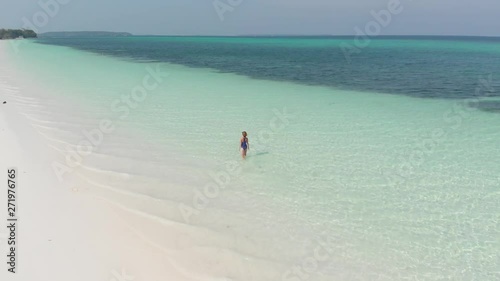 Aerial: Woman walking on white sand beach turquoise water tropical coastline Pasir Panjang Kei Islands Indonesia Moluccas Indonesia scenic travel destination. Native cinelike D-log color profile photo