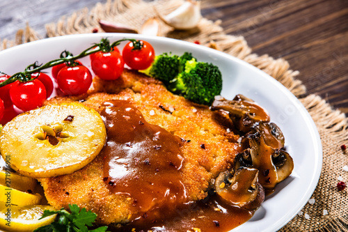 Fried pork chop with vegetables and mushrooms on wooden background