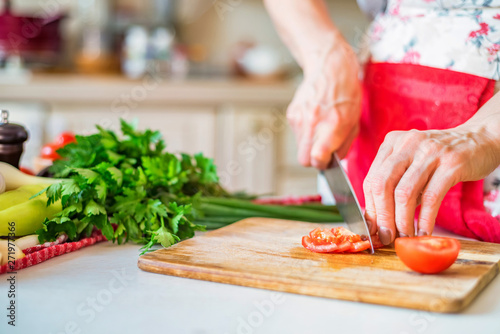 Female hand with knife chops tomato in kitchen. Cooking vegetables