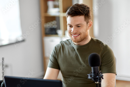 technology, mass media and podcast concept - happy young male audio blogger with laptop computer and microphone broadcasting at home office