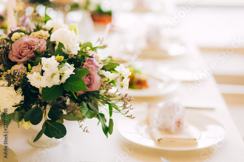 Gorgeous luxury wedding table arrangement  floral centerpiece close up. The table is served with cutlery  crockery and covered with a tablecloth. Wedding party decoration with pink and white flowers.