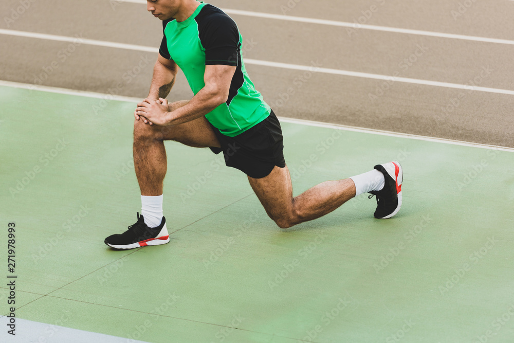 cropped view of mixed race sportsman stretching at stadium cropped view of mixed race sportsman stretching at stadium