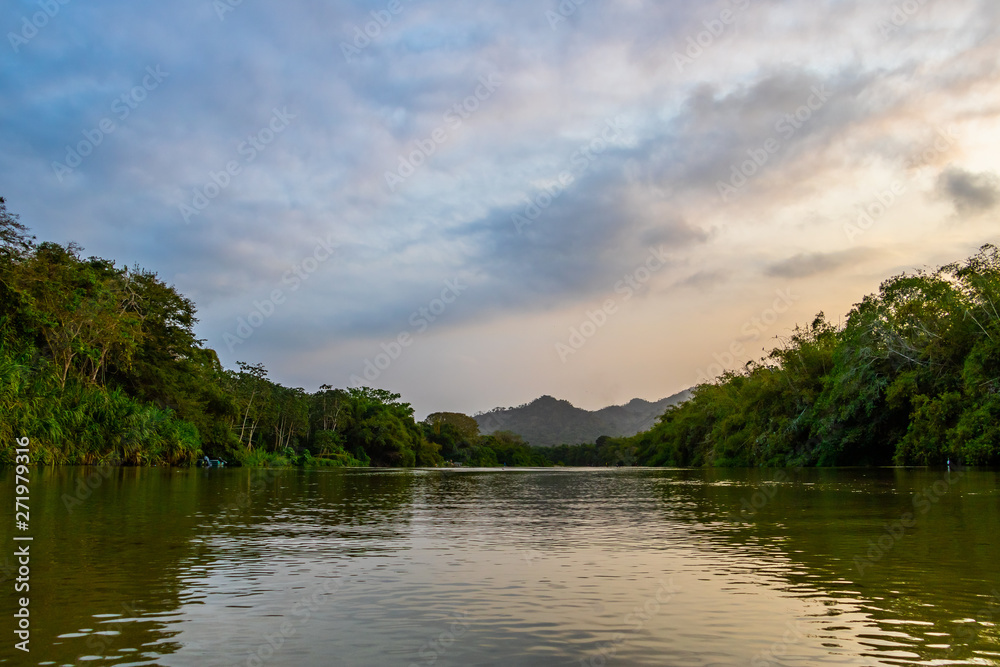 A wide, shallow river streams calmly through the deep South American jungle at blue violet dusk A wide, shallow river streams calmly through the deep South American jungle at blue violet dusk