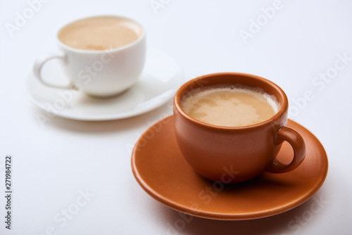 selective focus of coffee with foam in cups on saucers on white background