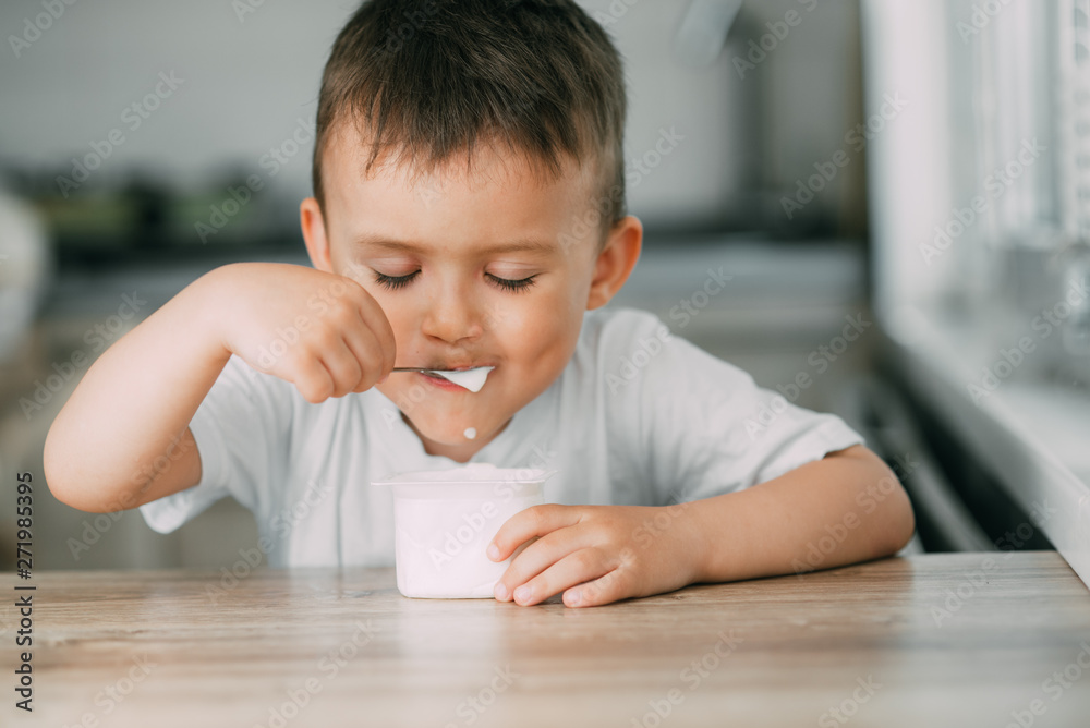 Adorable little boy eating yogurt in the kitchen in the afternoon Adorable little boy eating yogurt in the kitchen in the afternoon