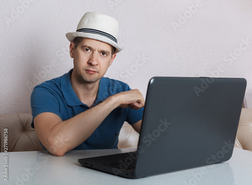 the man with the laptop sits at a table, looks in the camera