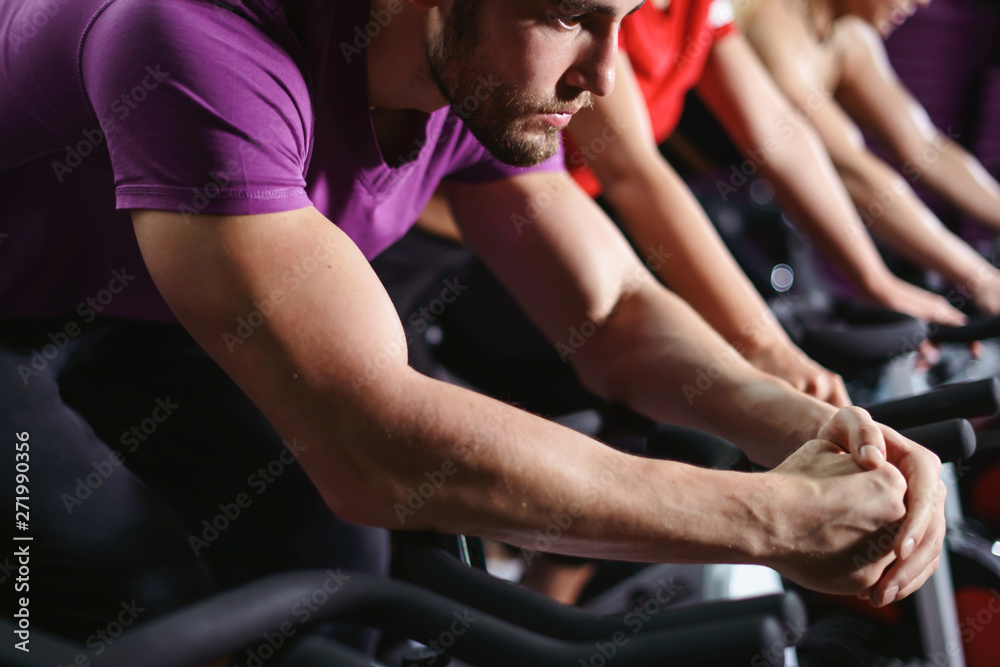 Close up hands of man biking in spinning class. Group of smiling friends at gym exercising on stationary bike. Happy cheerful athletes training on exercise bike. Close up hands of man biking in spinning class. Group of smiling friends at gym exercising on stationary bike. Happy cheerful athletes training on exercise bike.