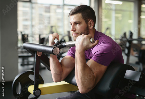 Young healthy sporty athletic man in the gym performing biceps curls with a barbell and doing arms exercises. Training in fitness studio