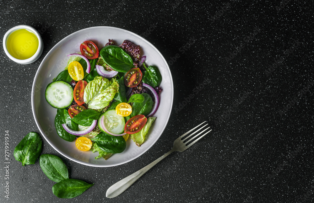 Top view of greens vegetable salad bowl with lettuce, spinach, cherry tomatoes, and red onion. Concept of healthy food, vegetarian and vegan food, fitness, sports, and lifestyle.