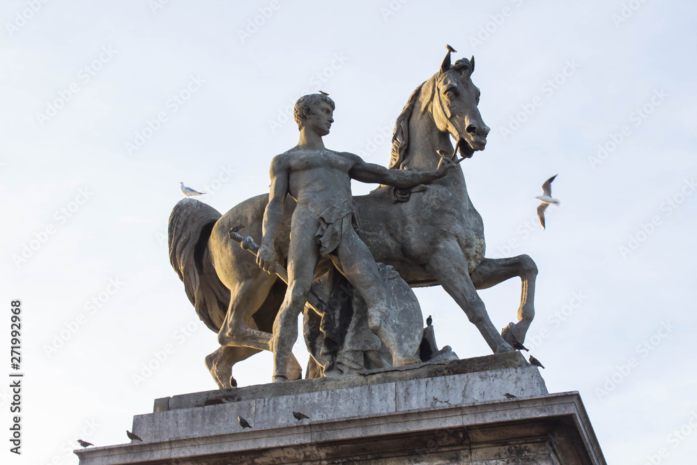 The statue near the bridge of a nude man with a sword in one hand and holding a horse by the bridles. Bright summer day and seagulls on a monument. Art and architecture in the Paris.