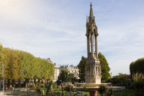 The garden in the park near Notre Dame de Paris and the tower in the Gothic architecture style in the middle of it. Sunny day in the center of Paris. Outdoor walking in the park and rest.