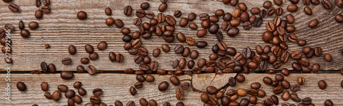 panoramic shot of wooden weathered table with scattered fresh roasted coffee beans