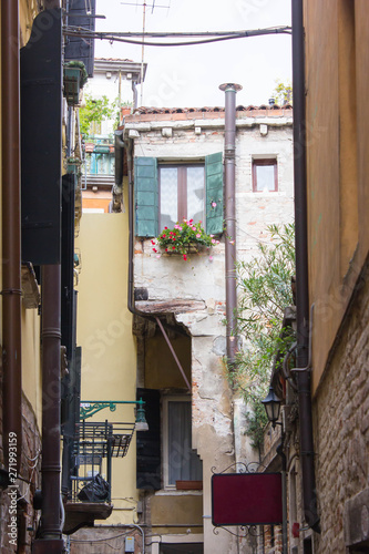 Courtyard of residential houses of the locals of Venice. Drainpipe on the facade and a balcony with flowers and shutters on the windows. Very narrow street  lane at the daytime. Non touristic place.